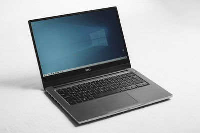 A Dell laptop with a blue desktop screen on a white surface, representing an affordable budget laptop
