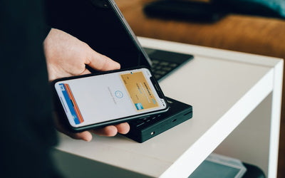 A person holding a smartphone over a payment terminal to make a contactless Apple Pay purchase