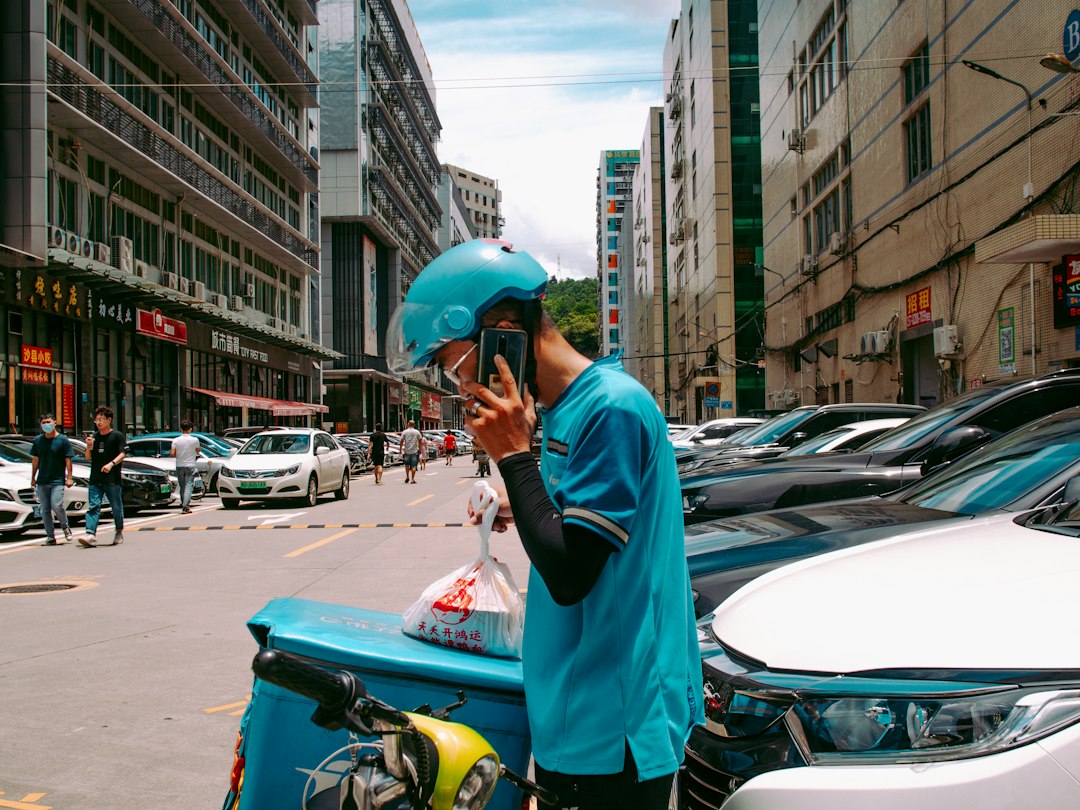 Delivery rider on a call beside parked vehicles, representing fast courier and quick-commerce delivery culture in India