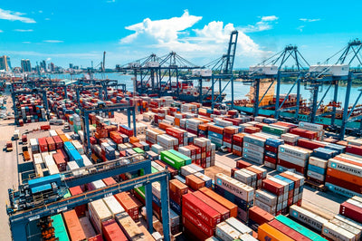 Shipping containers stacked at a busy port harbour, representing India's laptop and PC import restrictions